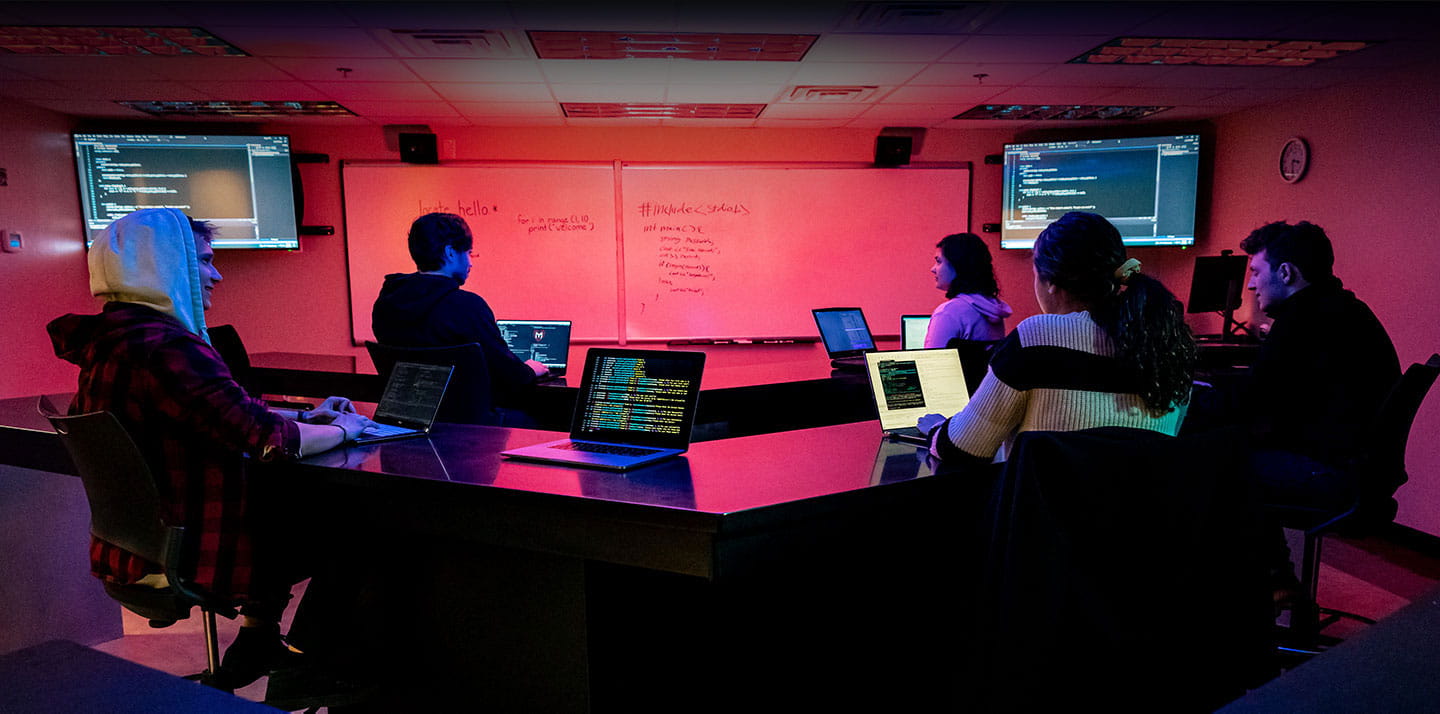 Students sit in a dark computer lab