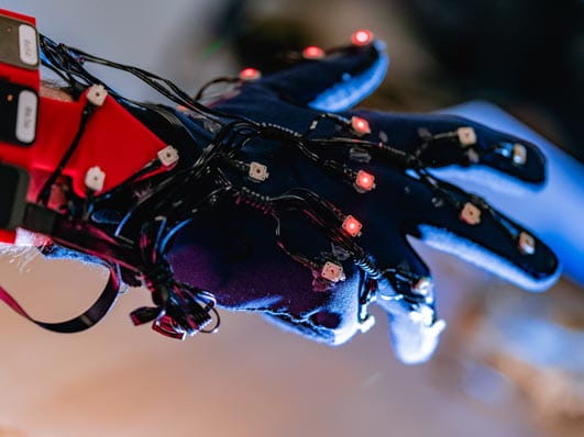 Close-up of a gloved hand fitted with sensors and small lights, used for motion capture or robotics research.