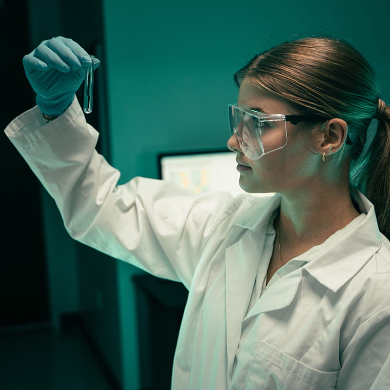 Embry-Riddle student in a lab coat and safety glasses holds a test tube up