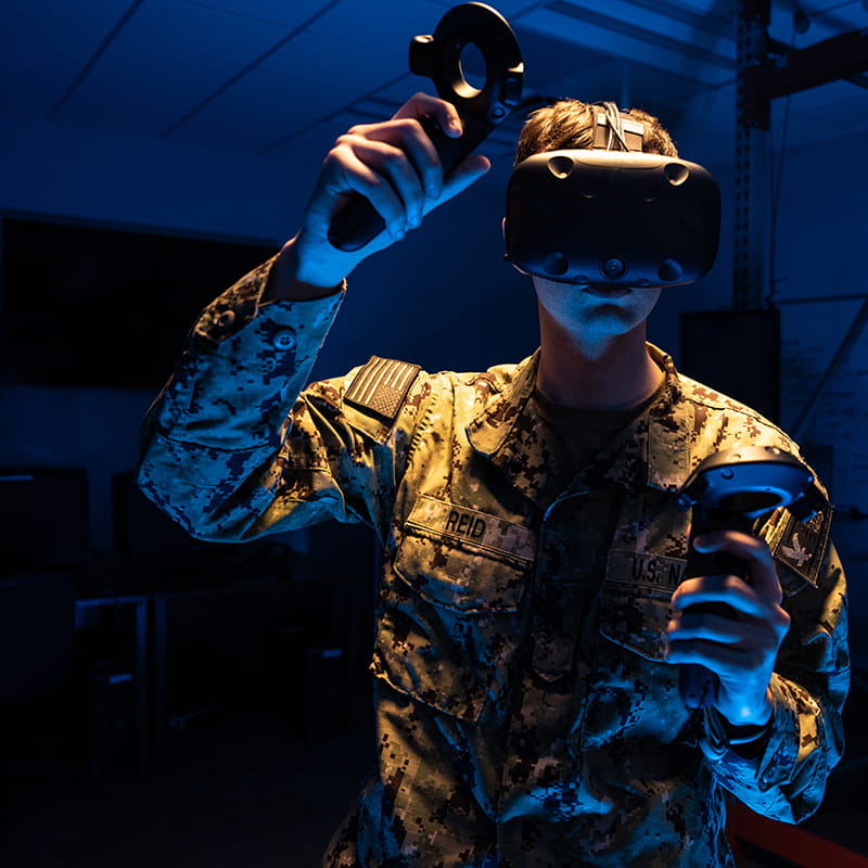 Embry-Riddle student in army fatigues wears virtual reality goggles and holds a controller