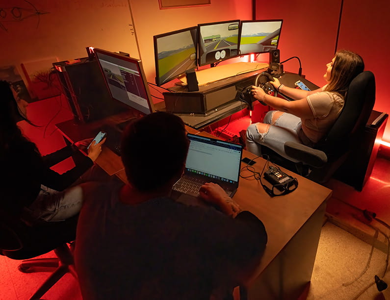A woman driving a simulator while two people look on in front of computers
