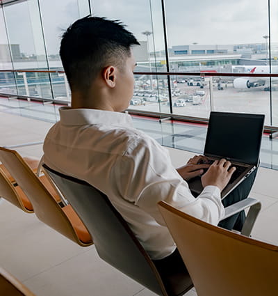 Embry-Riddle Worldwide student works on a laptop in an airport overlooking the tarmac