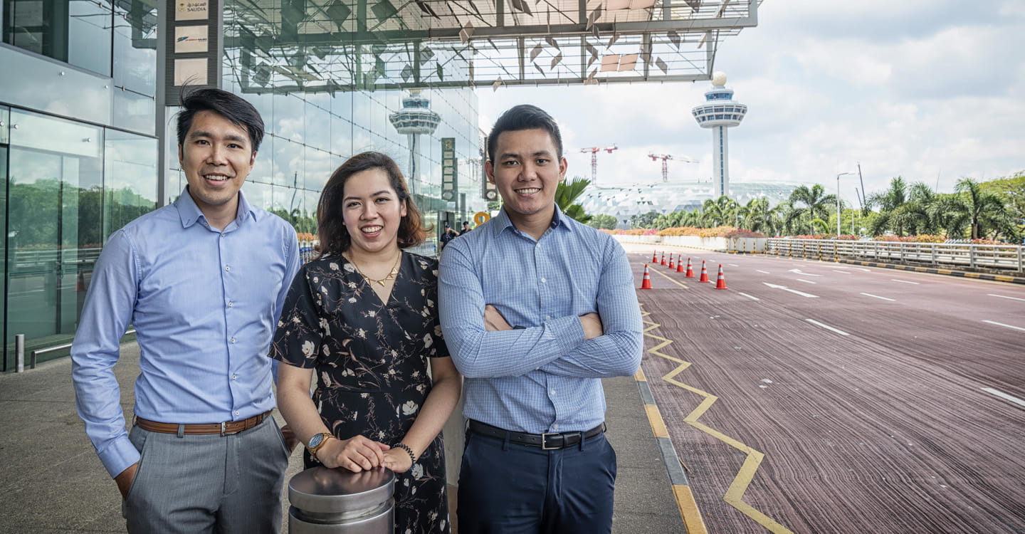 Three people standing outside of an airport.