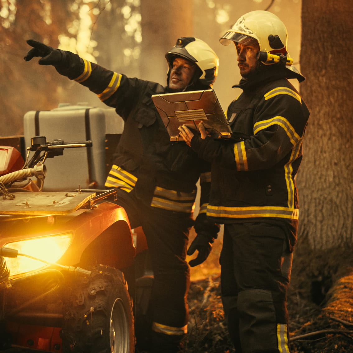 Firefighters stand next to an all terrain vehicle looking at a laptop