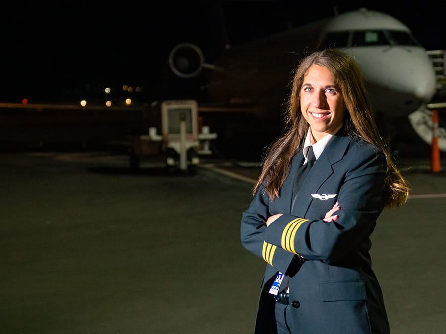 An Embry-Riddle flight instructor stands on the tarmac at night in front of a plane