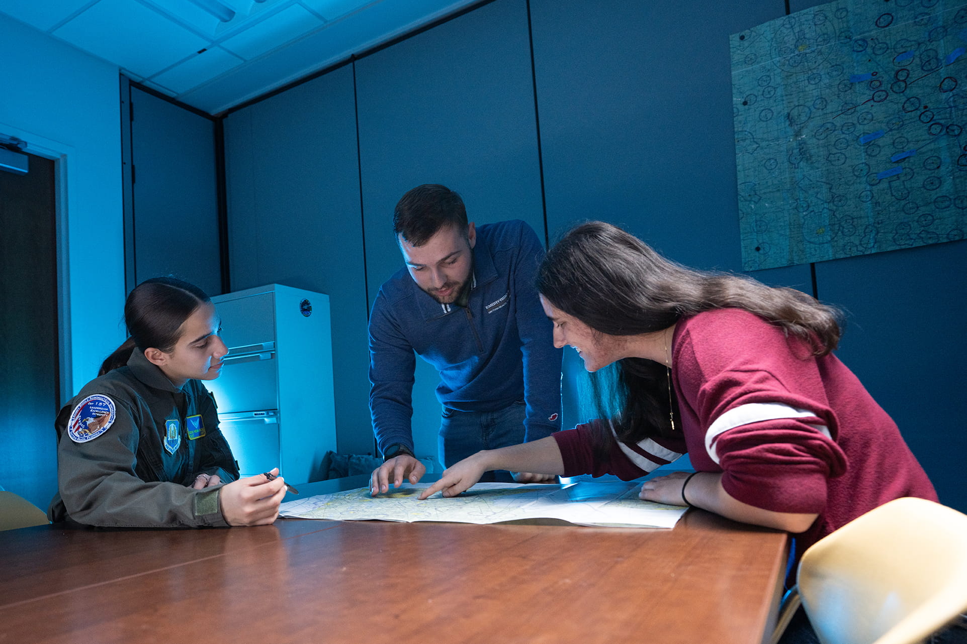 Three Embry-Riddle students gather around a table and look at flight maps