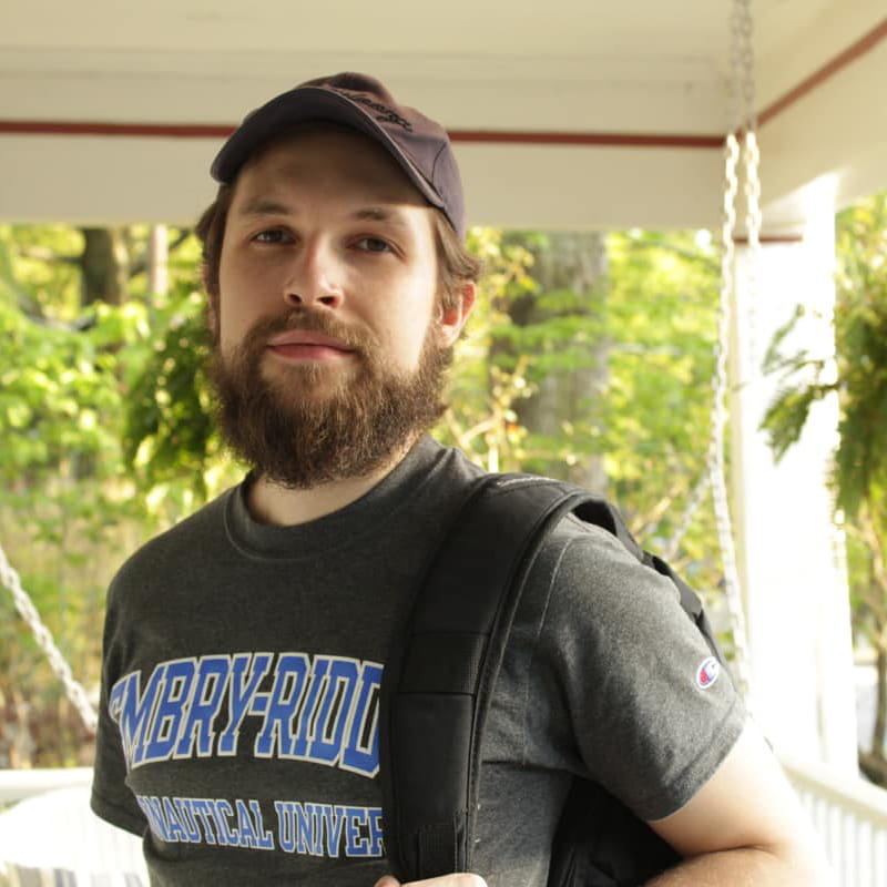 Lucas Miguel de Bail Ribas stands outside on a porch wearing an Embry-Riddle shirt