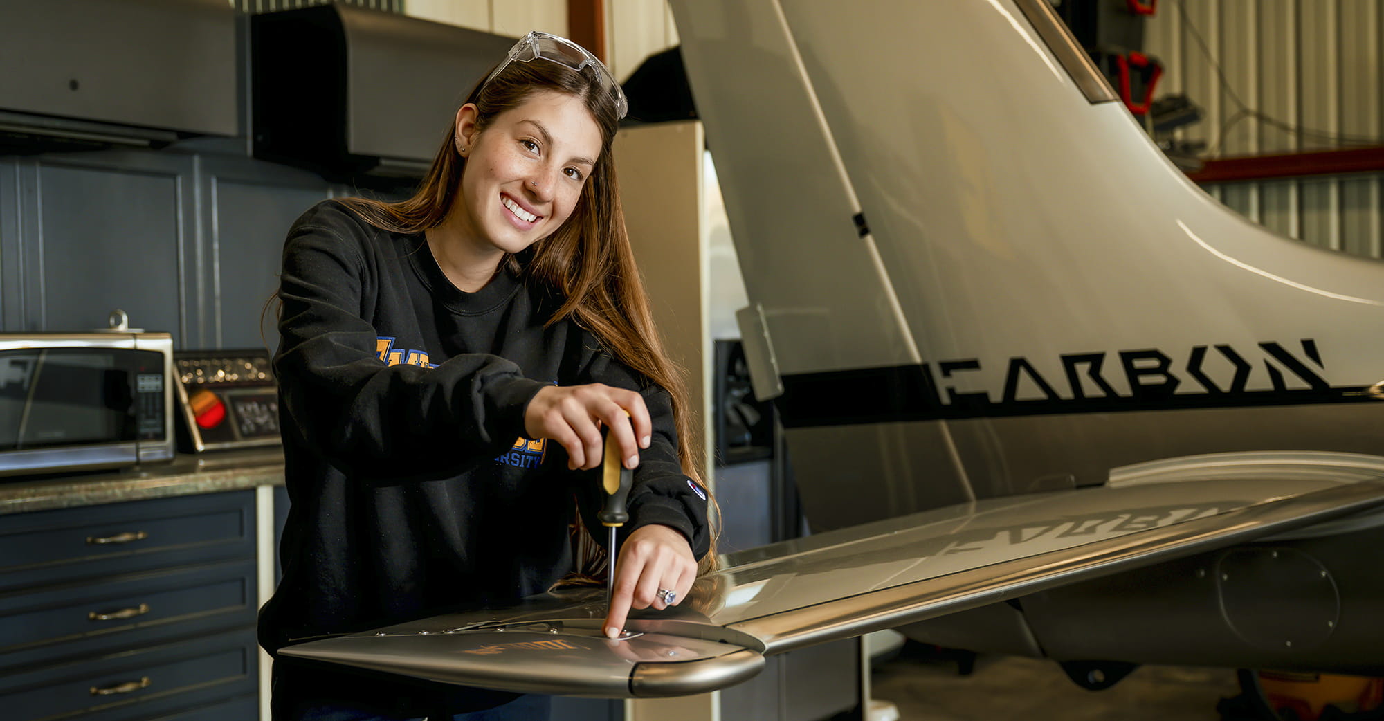 An Embry-Riddle student uses a screwdriver to repair a plane wing in a maintenance shop
