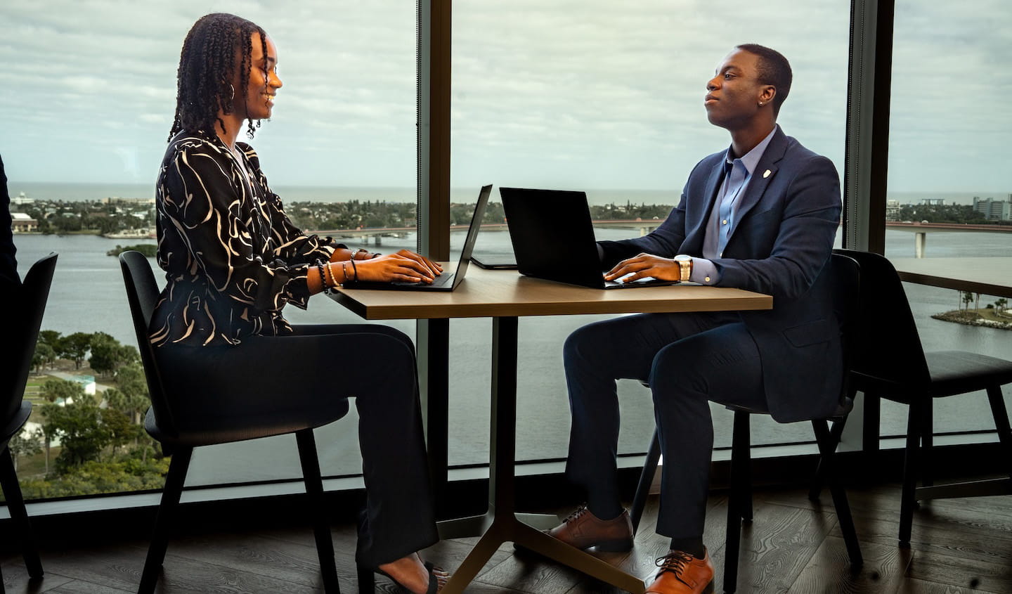 Two people sitting at a desk, working on laptops.