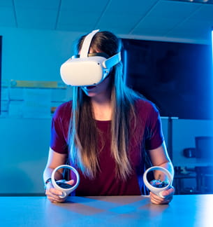 Student wearing a VR headset and holding controllers while interacting with a virtual environment in a lab.