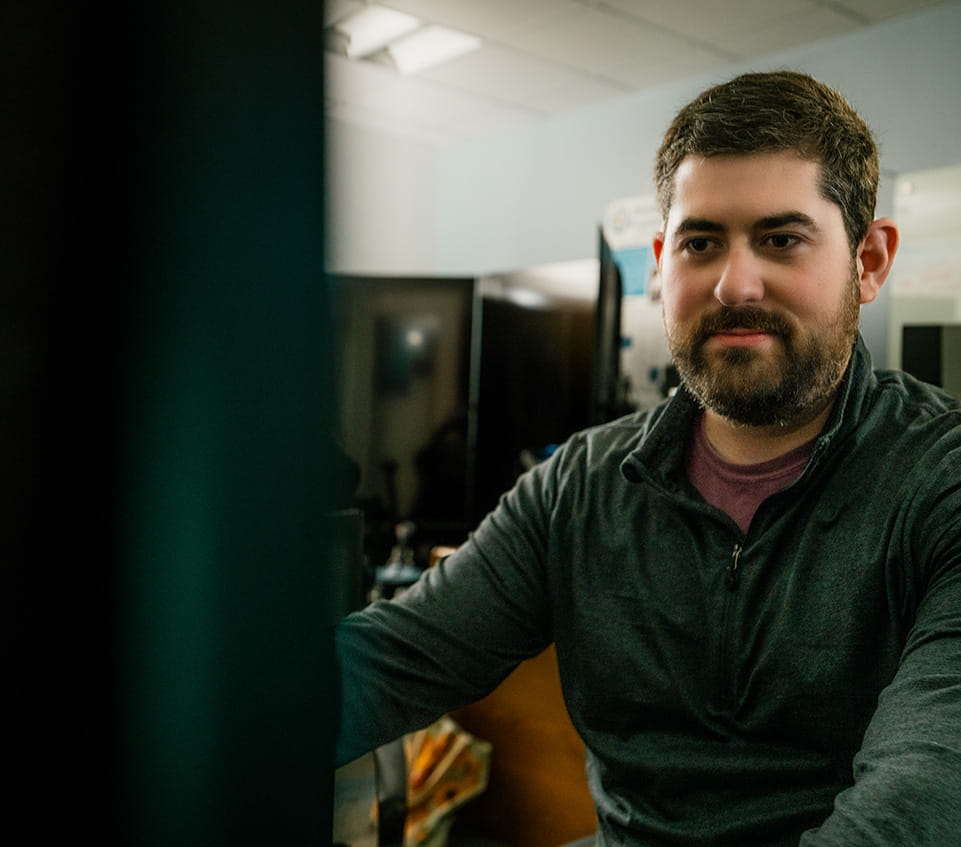 Student works at a computer workstation in a lab, focusing on a monitor with equipment and screens in the background.
