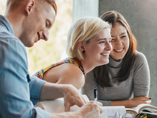 Three smiling students, sitting together at a desk.