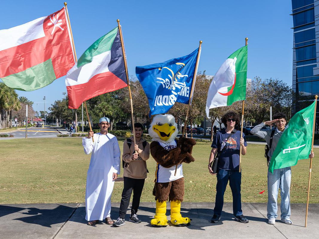 Students holding different flags alongside Ernie the Eagle