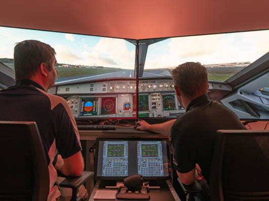 Two people sitting in the cockpit of an airplane.