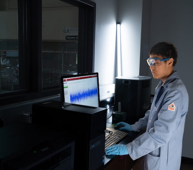 Student in a lab coat standing in front of a computer