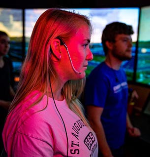 Two individuals stand in a control room operating air traffic control equipment.