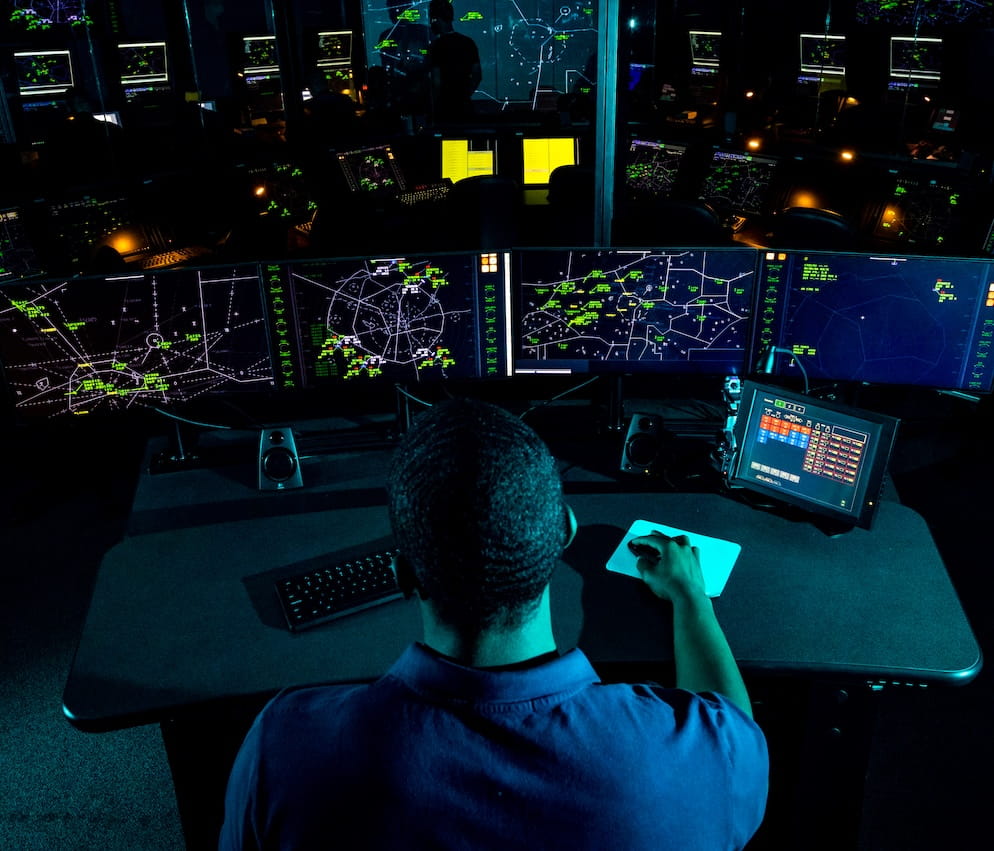 A person sits at a desk in an air traffic control room, using air traffic equipment.