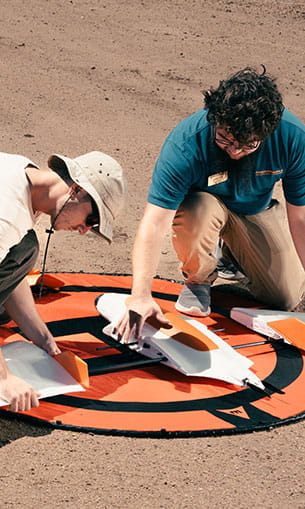 Two students kneel outside over a drone.