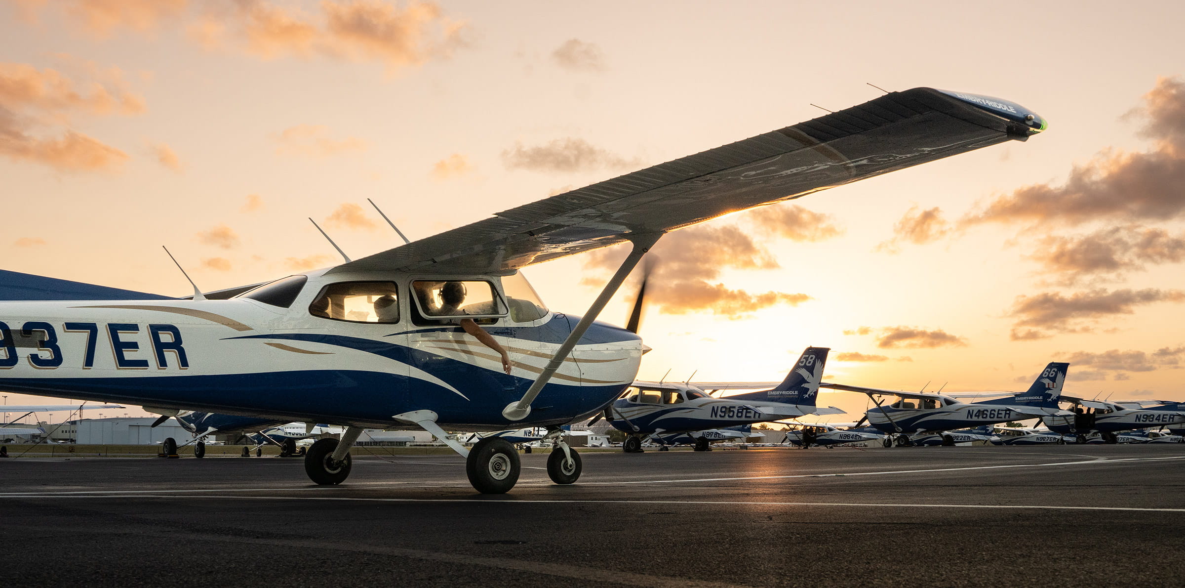 Small airplanes sitting on a runway at sunset.