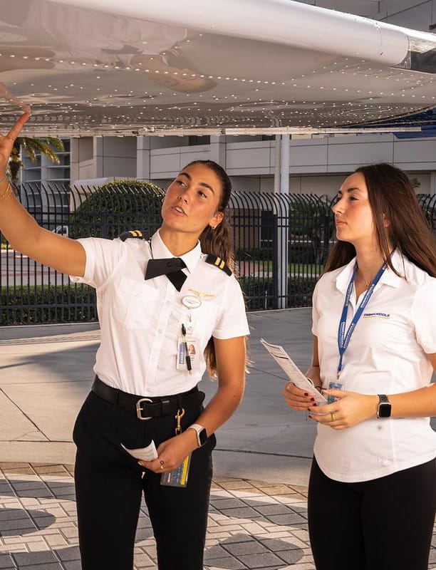 Two people looking at the underside of an airplane wing.