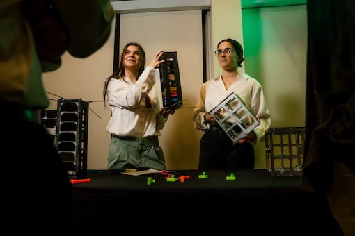 Two presenters demonstrate a device in a laboratory setting.