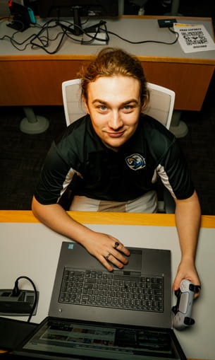 A person sits at a desk working on a laptop and looks up toward the camera.