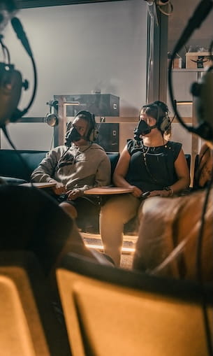 A group of people seated in a laboratory-like environment, wearing masks and headphones.