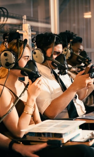 A group of people seated in a laboratory-like environment, wearing masks and headphones.