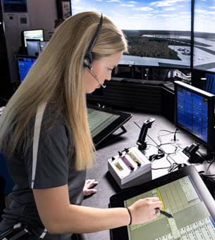 An individual with headphones on, working inside an air traffic control room.