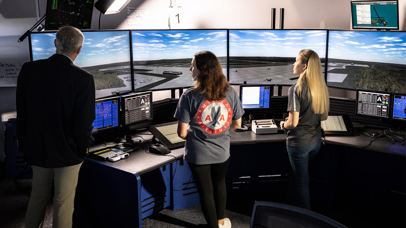 Three individuals in an air traffic control tower looking out over the runway.