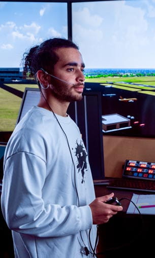 A person with headphones on, standing in an air traffic control room.