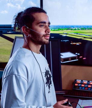A person with headphones on, standing in an air traffic control room.