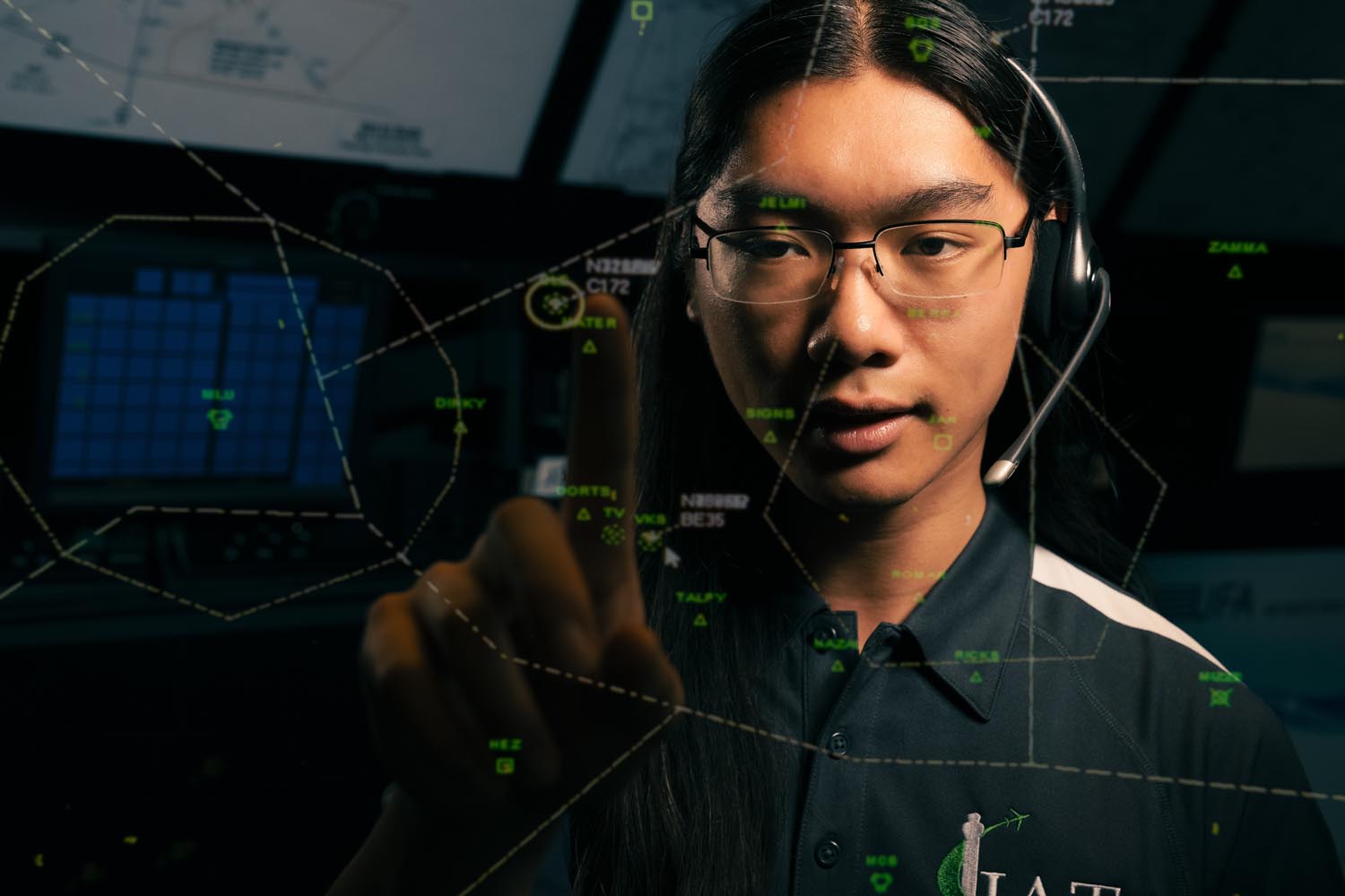 A person wearing a headset and glasses interacts with a digital air traffic control display, touching a point on the illuminated screen.