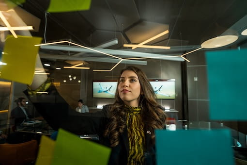A business professional looking at post-it notes on a glass wall.