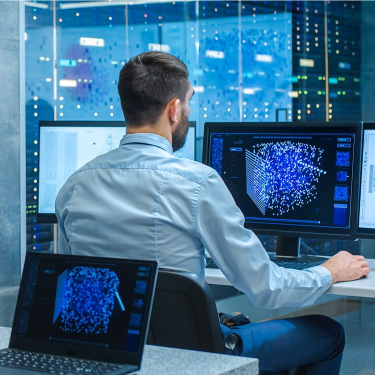 Student analyzing data visualization on computer monitors in technology lab with server racks in background.