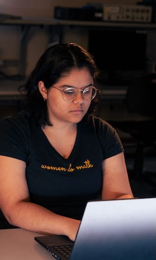 Student working on laptop in computer lab wearing t-shirt that reads, 'women do math.'