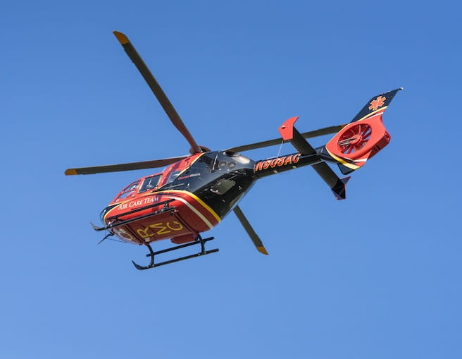 A black and red Air Care Team helicopter flying against a blue sky. 