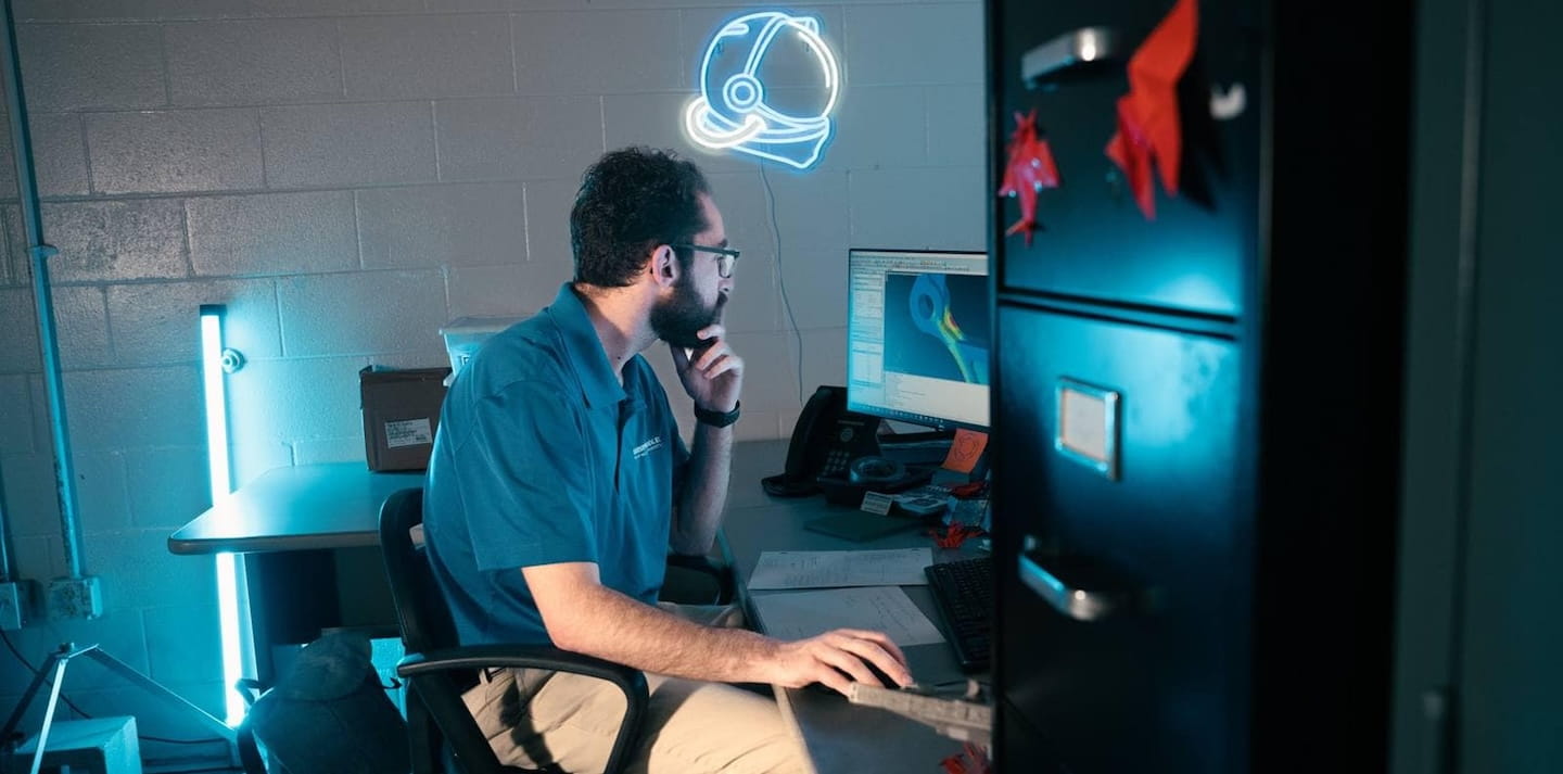 Researcher analyzes a computational simulation on a desktop monitor in a lab office with accent lighting and an aviation helmet neon sign on the wall.