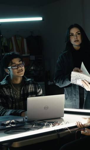 Two individuals working together on a computer in a classroom-style environment.