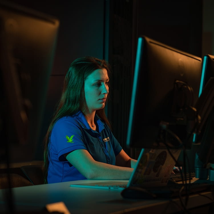 Student in an Embry-Riddle polo works at a desktop computer between two large monitors in a dimly lit lab with colored accent lighting.