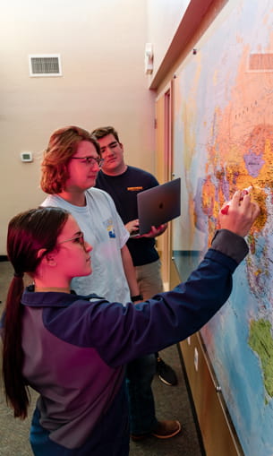 Three people work together on a large map pinned to a wall.