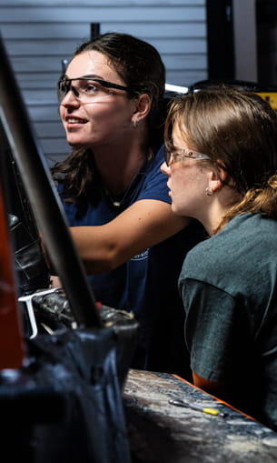 Two people wearing safety goggles, working on equipment in a laboratory setting.