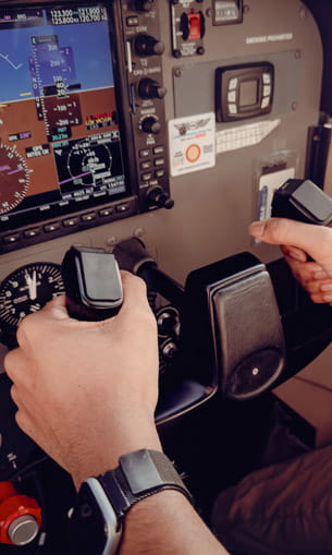 A close-up view inside a small aircraft cockpit showing a pilot’s hands on the controls.