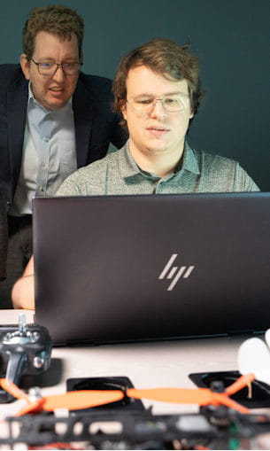 Student at laptop with teacher behind him.