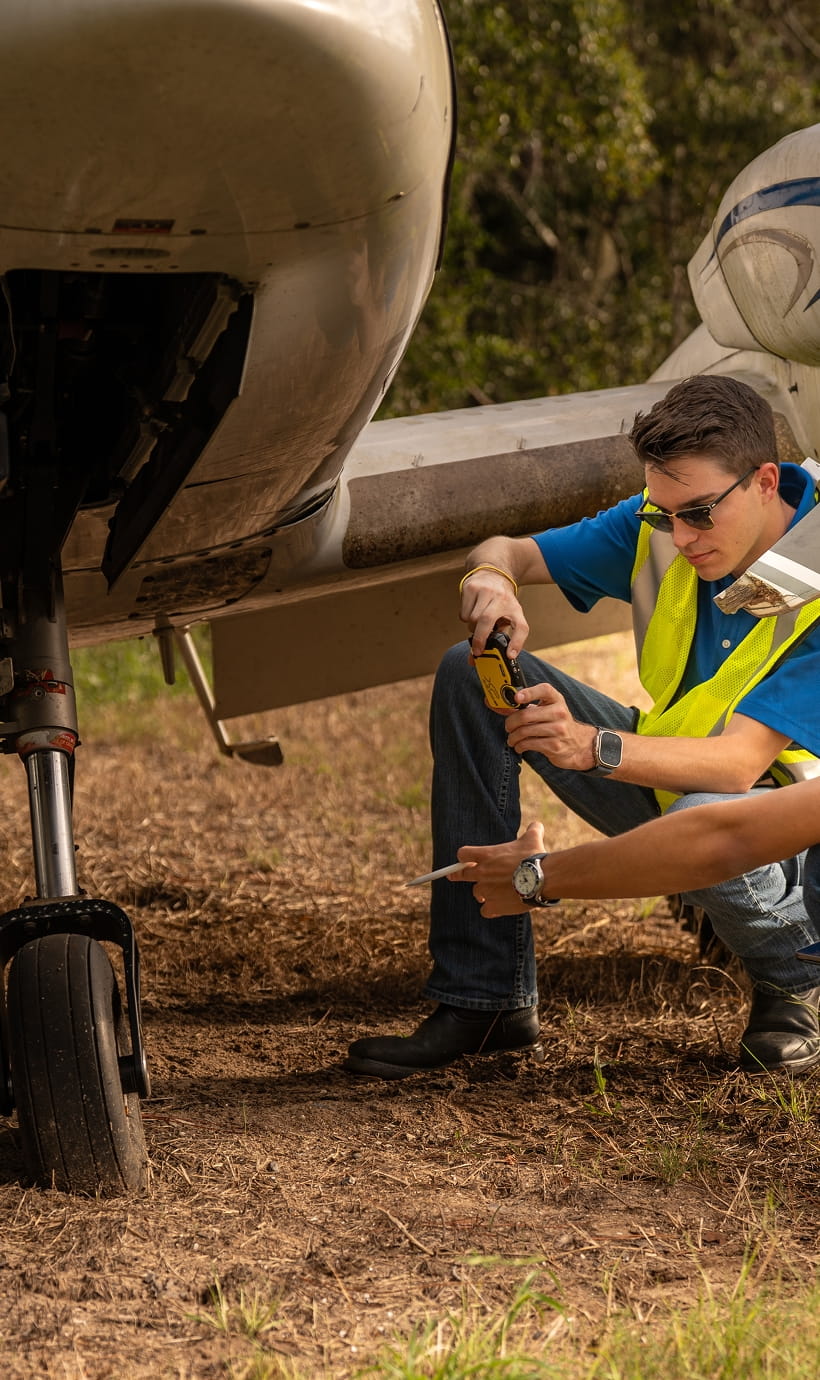 Two people crouched down beside an airplane, inspecting the aircraft.