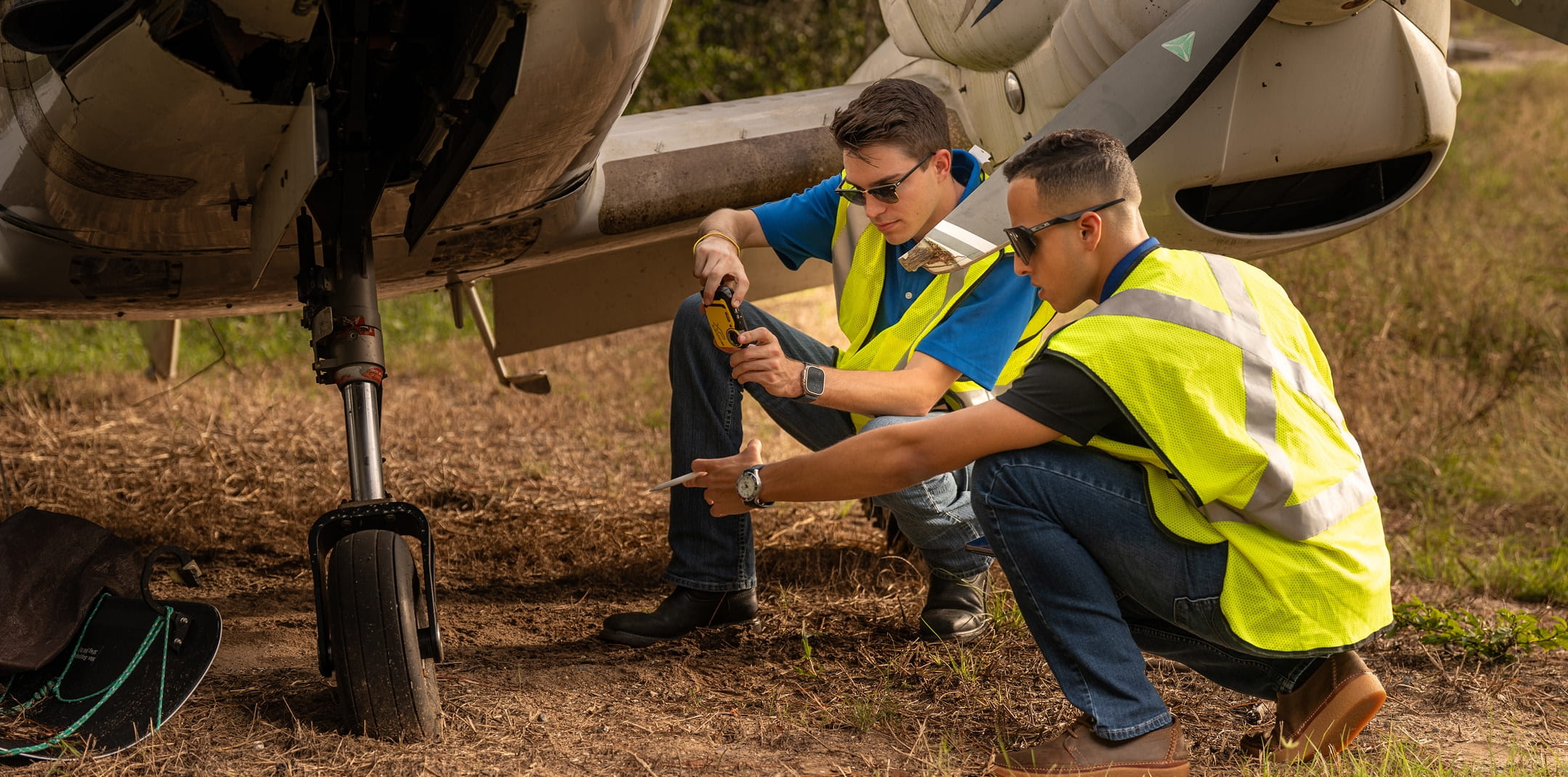 Two people crouched down beside an airplane, inspecting the aircraft.