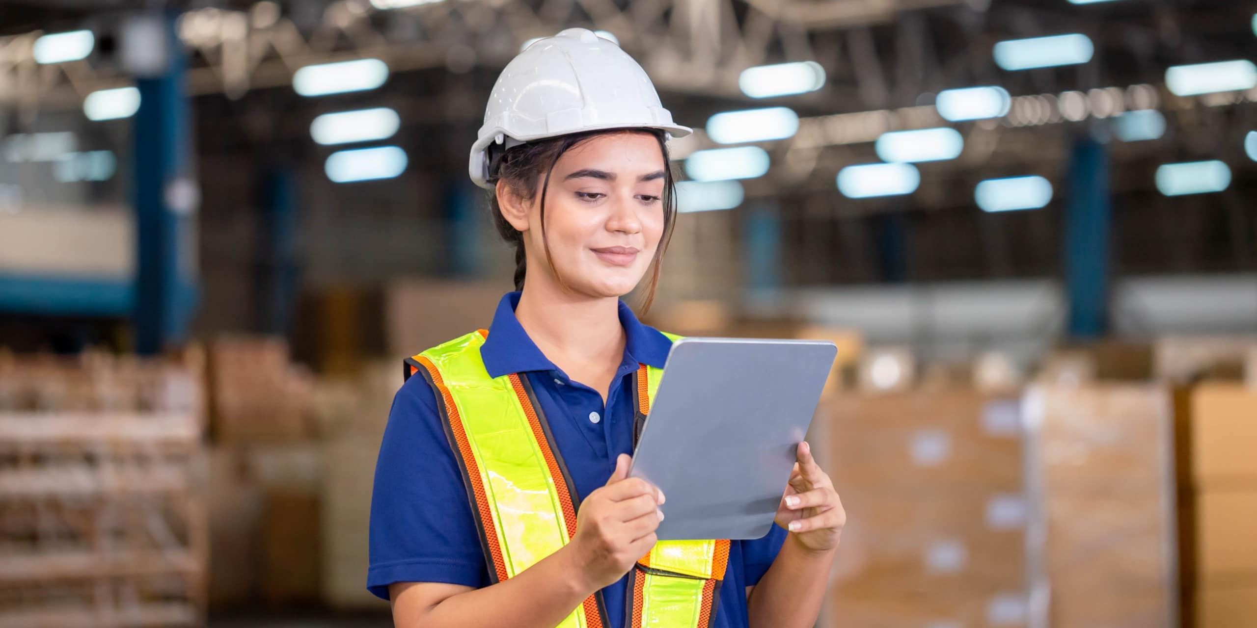 A person carrying a tablet while wearing safety equipment inside a factory.