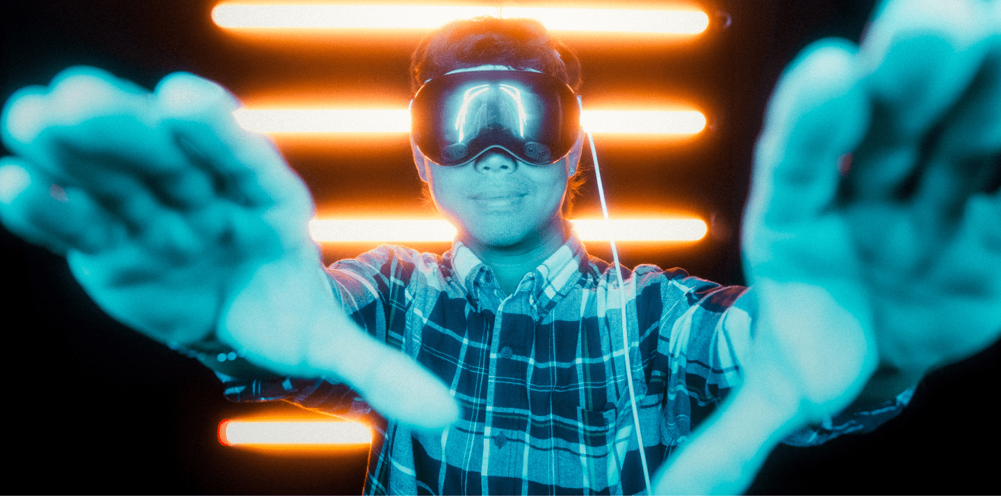 Student wearing a virtual reality headset reaches forward in an immersive lab setting with bright LED light bars in the background.
