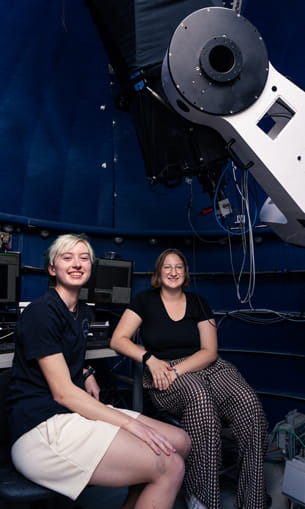Women sit by a telescope.