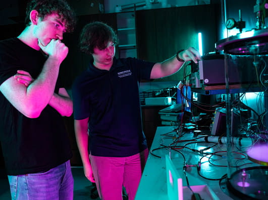 Three people work together in a laboratory, examining equipment under colorful lighting.